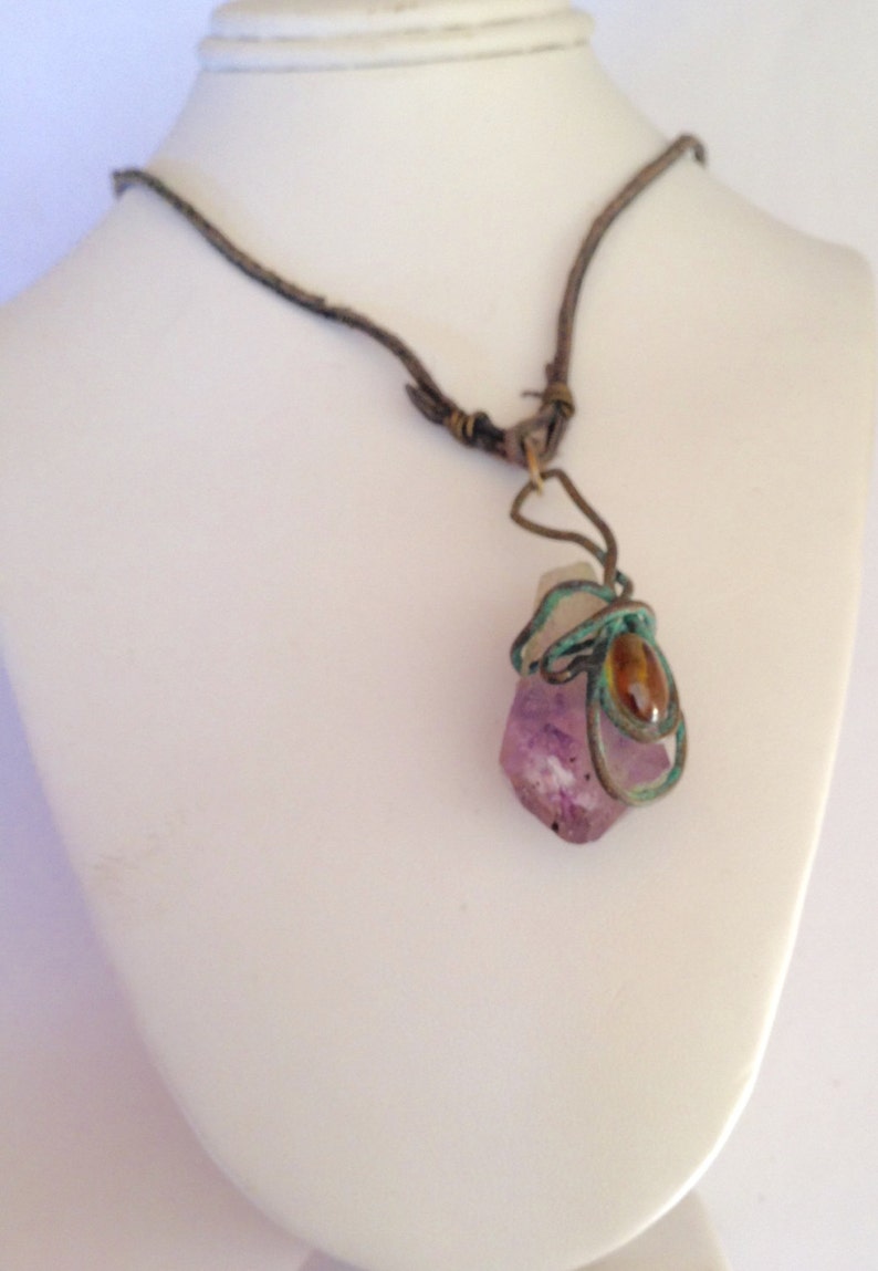 May include: A purple amethyst crystal wrapped in wire with a brown leather cord necklace.