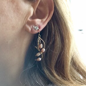 May include: A pair of gold dangle earrings with pink pearls and a clear crystal. The earrings are hanging from a woman's ear.
