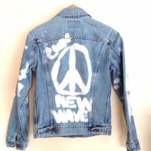 May include: A light blue denim jacket with a white peace sign and the words "NEW WAVE" painted on the back.