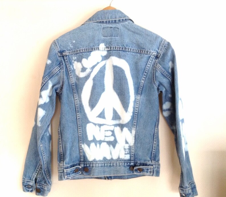 May include: A light blue denim jacket with a white peace sign and the words "NEW WAVE" painted on the back.