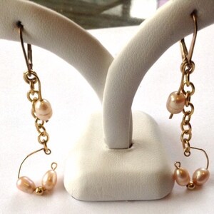 May include: A pair of gold earrings with a chain and three small pink pearls on each earring.