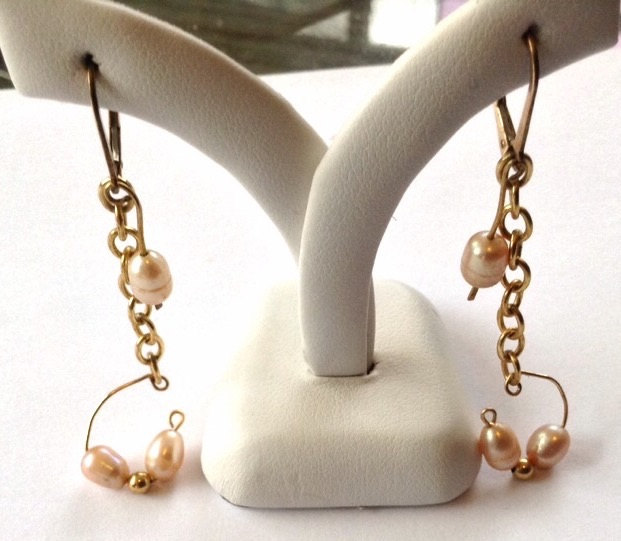 May include: A pair of gold earrings with a chain and three small pink pearls on each earring.
