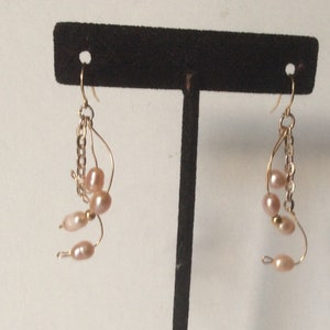May include: A pair of gold earrings with a chain and multiple pink pearls hanging from each earring.