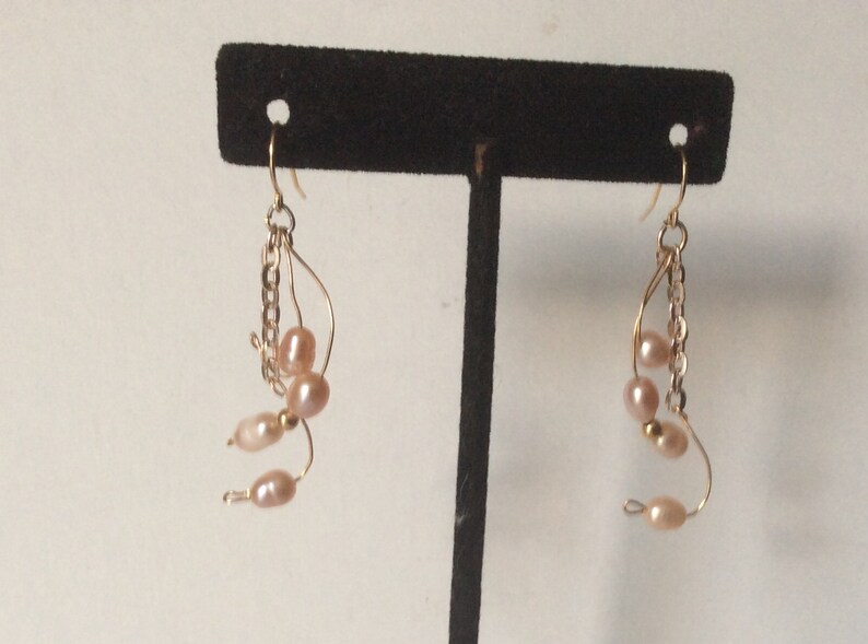 May include: A pair of gold earrings with a chain and multiple pink pearls hanging from each earring.