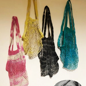 May include: Four colorful crocheted string bags hanging on a white wall. The bags are in shades of yellow, black, teal, and pink.