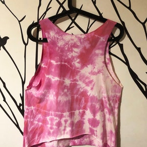 May include: Pink tie-dye tank top with a white background. The tank top is hanging on a black hanger.