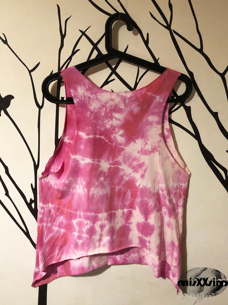 May include: Pink tie-dye tank top with a white background. The tank top is hanging on a black hanger.