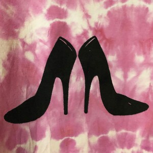 May include: A pair of black high-heeled shoes are printed on a pink and white tie-dye t-shirt.