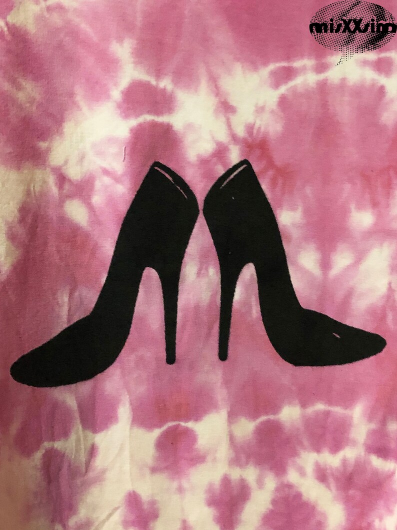 May include: A pair of black high-heeled shoes are printed on a pink and white tie-dye t-shirt.
