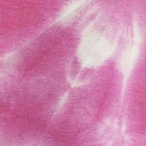 May include: A close-up of a pink and white tie-dye fabric. The fabric has a soft, textured feel and a subtle sheen.