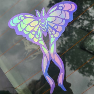May include: A holographic iridescent sticker of a moth with wings spread out. The moth is a light purple color with a green and blue iridescent sheen.