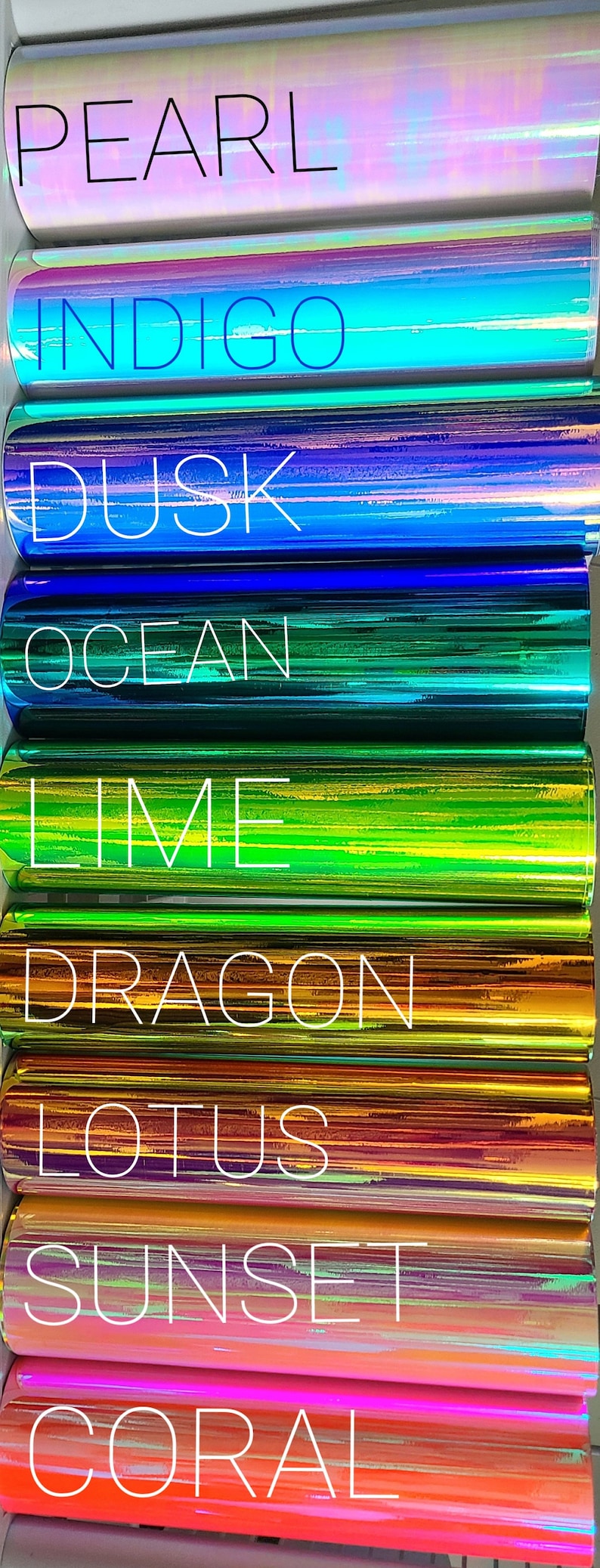 May include: A vertical image showcasing rolls of iridescent vinyl in various colors. Each roll is labeled with a color name in white text, including "PEARL", "INDIGO", "DUSK", "OCEAN", "LIME", "DRAGON", "LOTUS", "SUNSET", and "CORAL".