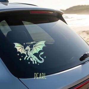 May include: A holographic dragon sticker with iridescent wings and star accents is displayed on a car window. The word "PEARL" is printed in a light green color below the dragon. The sticker is designed to be applied to a vehicle.