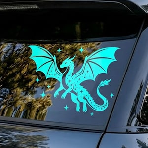 May include: A teal dragon decal with outstretched wings and star accents. The dragon is depicted in a stylized, fantasy art style, with a detailed body and wings. The decal is applied to a car window, creating a striking visual.