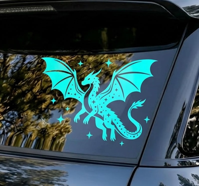 May include: A teal dragon decal with outstretched wings and star accents. The dragon is depicted in a stylized, fantasy art style, with a detailed body and wings. The decal is applied to a car window, creating a striking visual.
