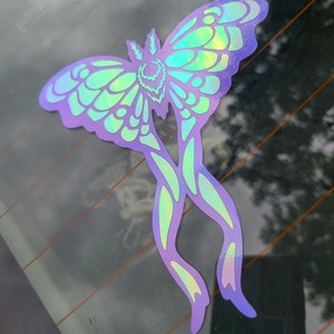 May include: A holographic iridescent sticker of a moth with a green and purple color scheme. The moth has a large wingspan and intricate details.