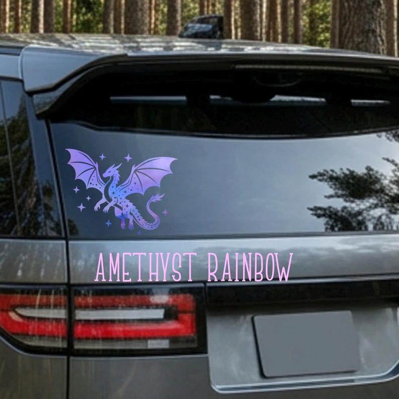 May include: A purple and blue dragon decal with outstretched wings and stars is affixed to the rear window of a vehicle. The text "AMETHYST RAINBOW" is below the dragon. The decal is likely for car decoration.