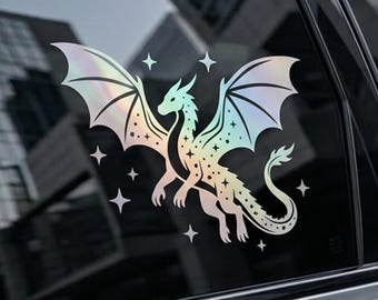 May include: A holographic dragon sticker with outstretched wings and star accents. The dragon is depicted in a detailed, stylized design, with a gradient of colors. The sticker is applied to a car window.