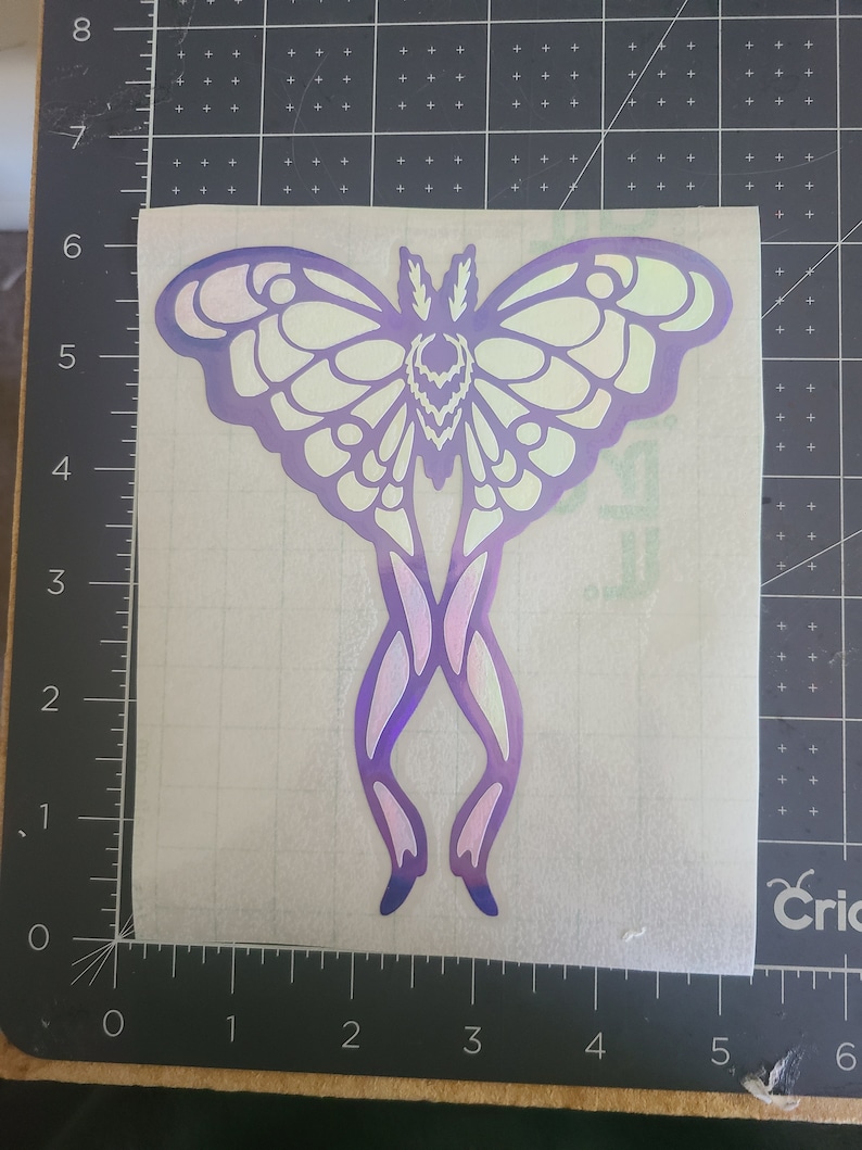 May include: A white and purple iridescent vinyl sticker of a moth with intricate wing details.