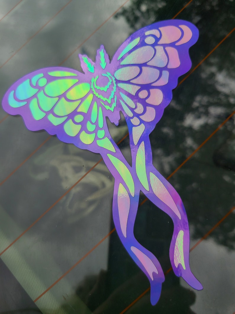 May include: A holographic iridescent butterfly sticker with a purple, green, and blue color scheme. The butterfly has intricate wing patterns and is in a flying pose.