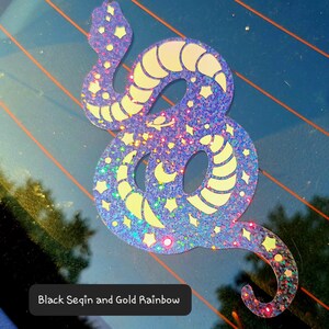 Pode incluir: Um adesivo de cobra azul iridescente brilhante com estrelas douradas de glitter e uma lua crescente. O adesivo diz "Black Sequin and Gold Rainbow".