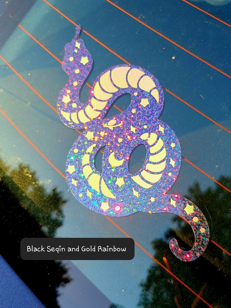 Pode incluir: Um adesivo de cobra azul iridescente brilhante com estrelas douradas de glitter e uma lua crescente. O adesivo diz "Black Sequin and Gold Rainbow".