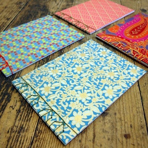 Peut inclure: Quatre petits carnets faits &agrave; la main avec des couvertures &agrave; motifs diff&eacute;rents. Les couvertures sont bleues avec des &eacute;toiles blanches, bleues avec des motifs floraux dor&eacute;s, roses avec un motif g&eacute;om&eacute;trique et violettes avec un motif paisley.