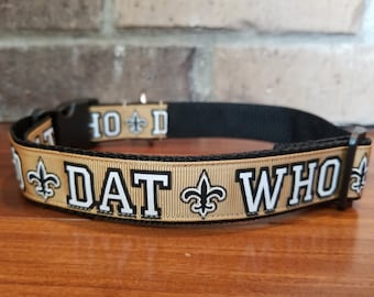 Könnte beinhalten: Ein gold-schwarzes Hundehalsband mit dem Text "DAT WHO" und Fleur-de-lis-Symbolen.