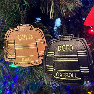 May include: Two Christmas ornaments shaped like sweaters with the text "CVFD SELL" and "DCFD CARROLL" on them. The ornaments are made of leather and have a black and tan striped pattern.