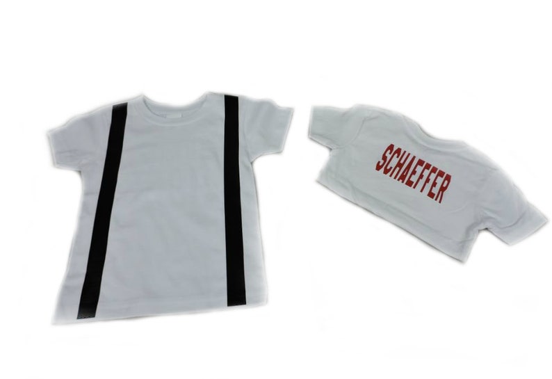 May include: Two white t-shirts. One has two vertical black stripes, resembling suspenders. The other shirt is smaller and has the name "SCHAEFFER" printed in red block letters.
