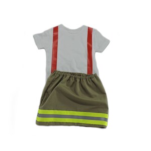 May include: A white t-shirt with red suspenders and a green skirt with yellow reflective stripes. The skirt has an elastic waistband.