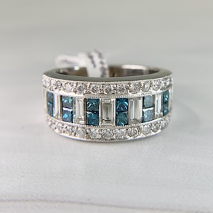 May include: A wide, silver-toned ring with a band of alternating blue and clear rectangular stones. The ring is encrusted with small, round, clear stones along the top and bottom edges. A white tag is attached to the ring.