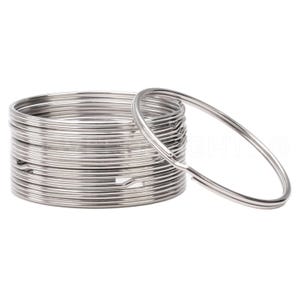 May include: A stack of silver metal key rings. The rings are stacked on top of each other and one ring is laying flat on the surface.