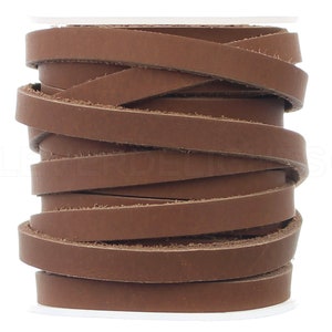 May include: A roll of brown leather cord, approximately 1/4 inch wide, is wound around a white spool. The leather cord is a natural brown color and has a smooth, polished finish.