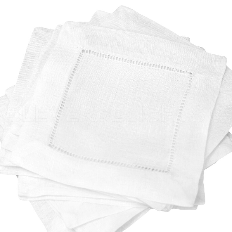 May include: A stack of white linen napkins with a delicate embroidered border. The napkins are folded and ready for use.