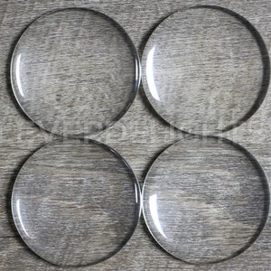 May include: Four clear glass circles, each with a smooth, reflective surface, are arranged in a square pattern on a woodgrain background.