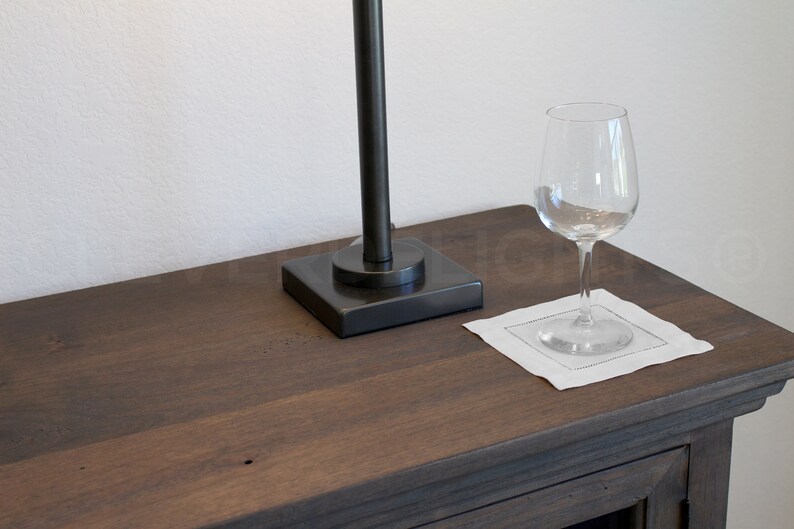 May include: A dark brown wooden table top with a black lamp and a clear wine glass on a white linen napkin.