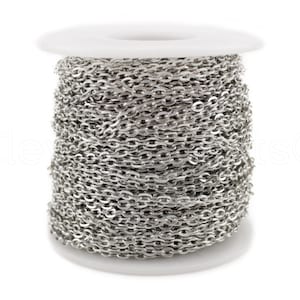 May include: A spool of silver chain, wound tightly around a white plastic spool. The chain is a simple, linked design.