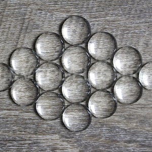 May include: A group of 13 clear glass marbles arranged in a diamond shape on a wood surface.