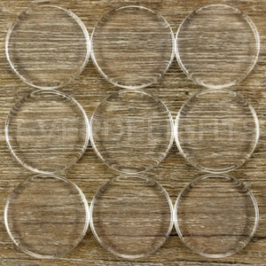 May include: Nine clear round glass or plastic discs arranged in a 3x3 grid on a wood surface.