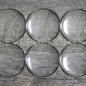 May include: Six clear glass circles, each with a smooth, reflective surface. The circles are arranged in two rows of three, with the top row slightly offset from the bottom row. The circles are all the same size and shape.