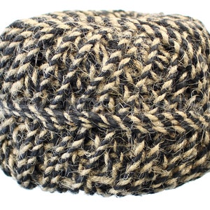 May include: A tightly woven, cylindrical basket made of natural jute rope. The rope is a mix of black and tan, creating a textured, patterned surface. The basket is likely used for storage or decoration.