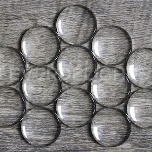 May include: A group of 12 clear glass cabochons arranged in a circular pattern on a wood surface.