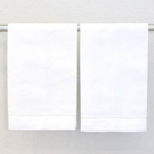 May include: Two white hand towels with a delicate embroidered border hang on a silver towel rack.