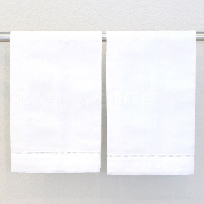 May include: Two white hand towels with a delicate embroidered border hang on a silver towel rack.