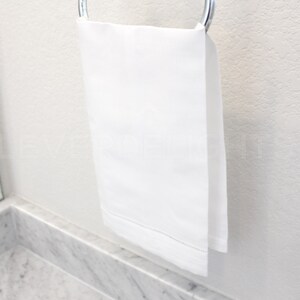 May include: A white bath towel hanging on a silver towel rack.