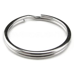 May include: A silver key ring with a double loop design. The ring is made of metal and has a smooth finish.