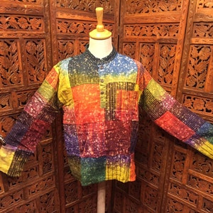 May include: A colourful patchwork long-sleeved shirt with a button-up collar. The shirt is made of a soft, lightweight fabric and features a variety of colours, including red, orange, yellow, green, blue, and purple.
