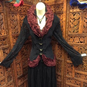 May include: A black and burgundy ruffled top with a lace overlay and a decorative buckle closure. The top is paired with black pants.