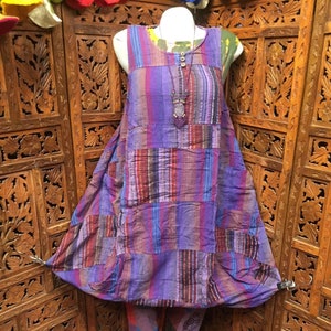 May include: A purple and blue striped patchwork dress with a button closure and a beaded necklace. The dress is on a mannequin and has a loose, flowing fit.
